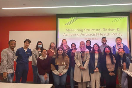 A group of learners poses in front of a presentation screen.