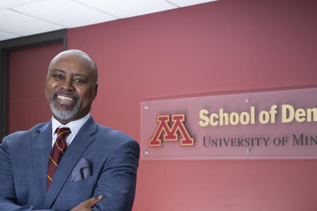 Dean Keith A Mays DDS MS PHD in front of a logo of the School of Dentistry