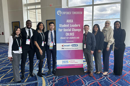 A group of students pose in front of a banner at ADEA