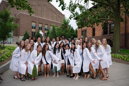 Students pose and celebrate wearing their white coats