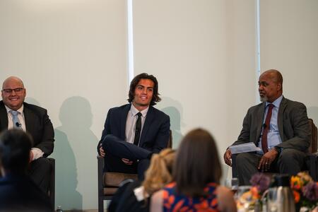 Armstrong speaks in front of the audience at Summer Celebration of Donors, while Alex Petronio and Keith Mays look o