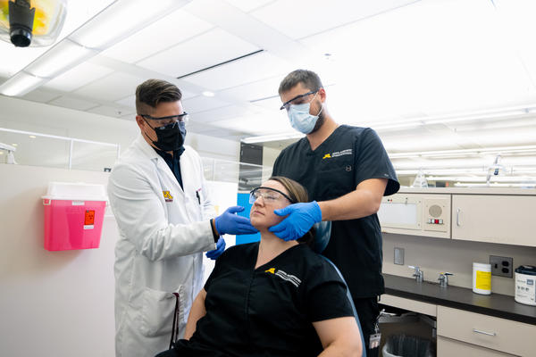 two dental therapy students inspect another students jaw during a demonstration