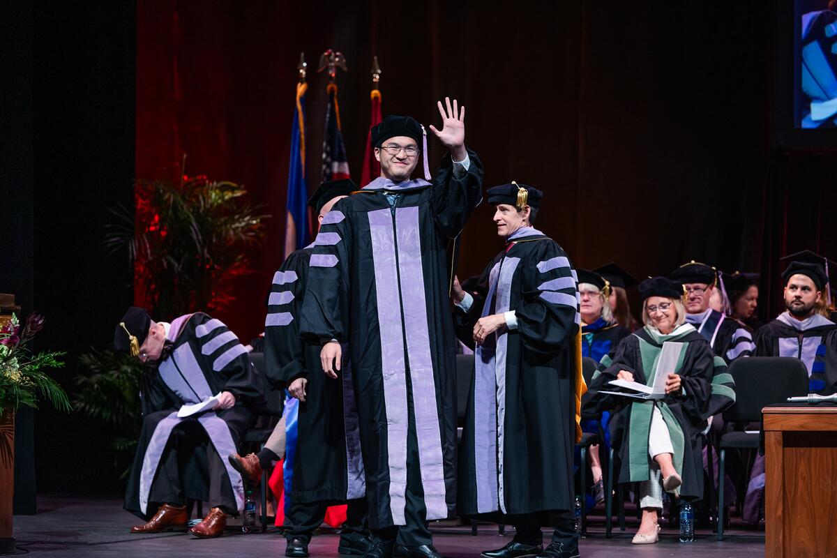 A graduate is hooded onstage and waves to the audience