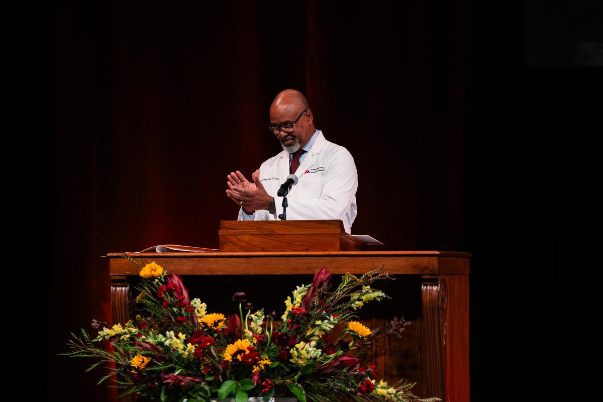 Dean Mays smiles and applauds from the podium