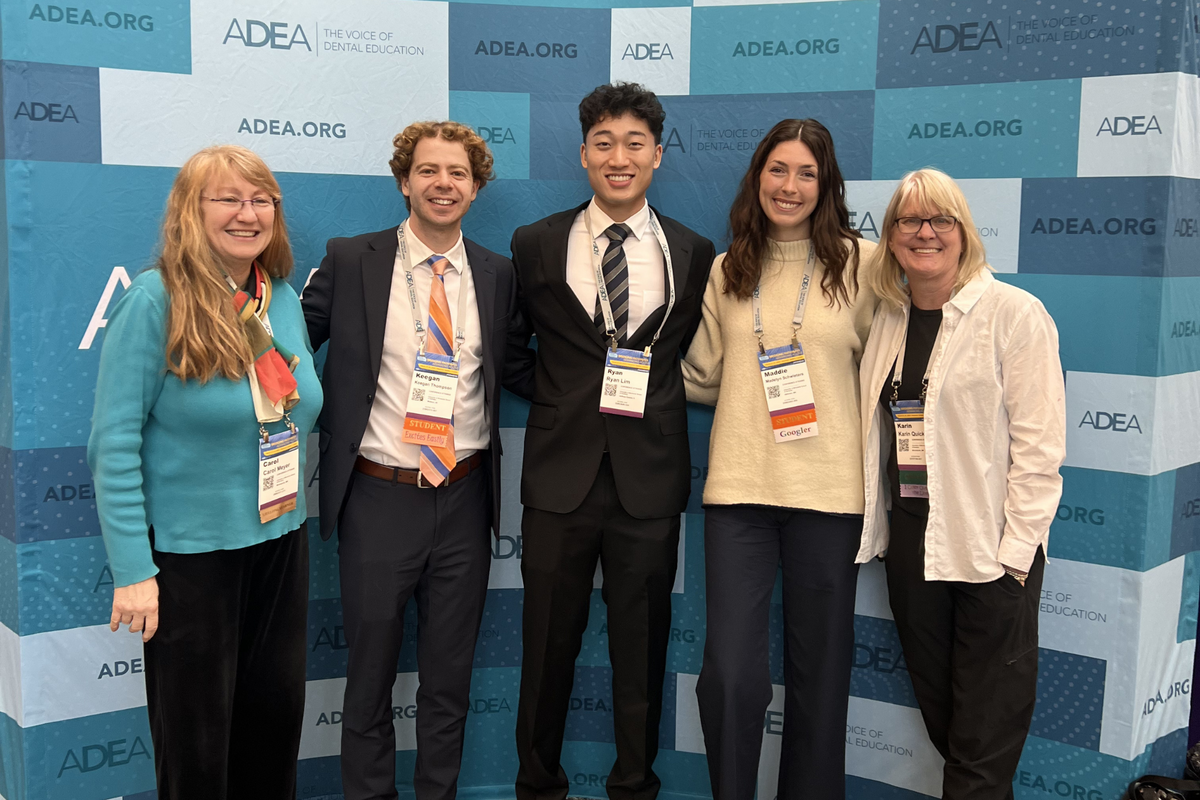 Students and faculty pose in front of an ADEA banner