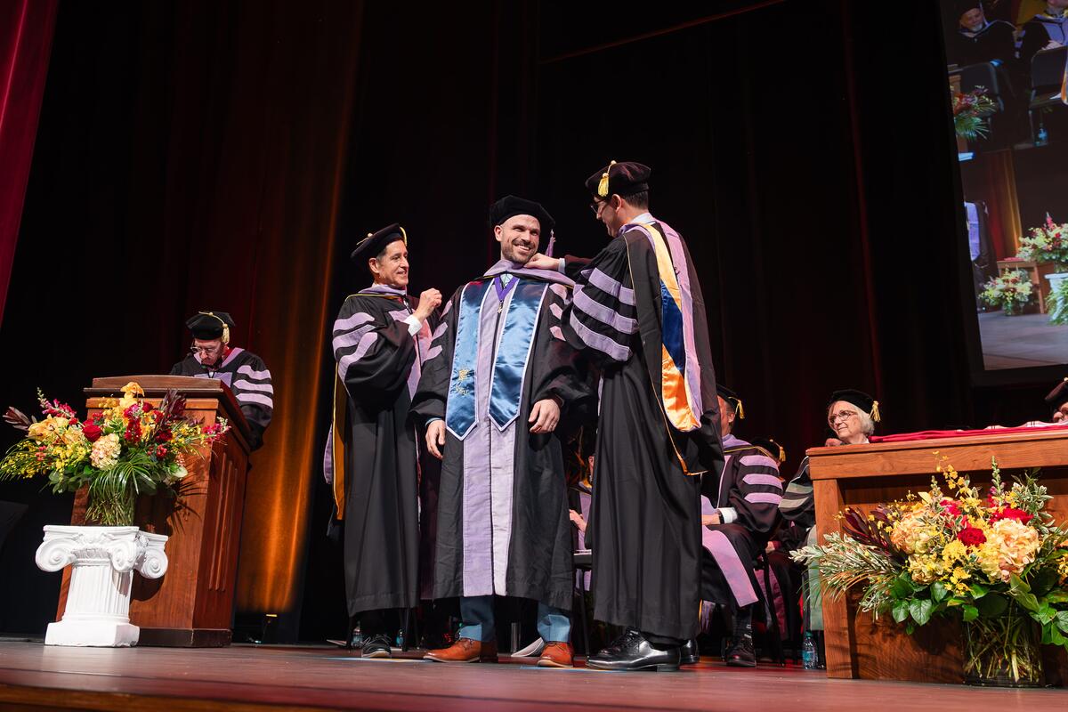 Graduate smiles as he receives his doctoral hood