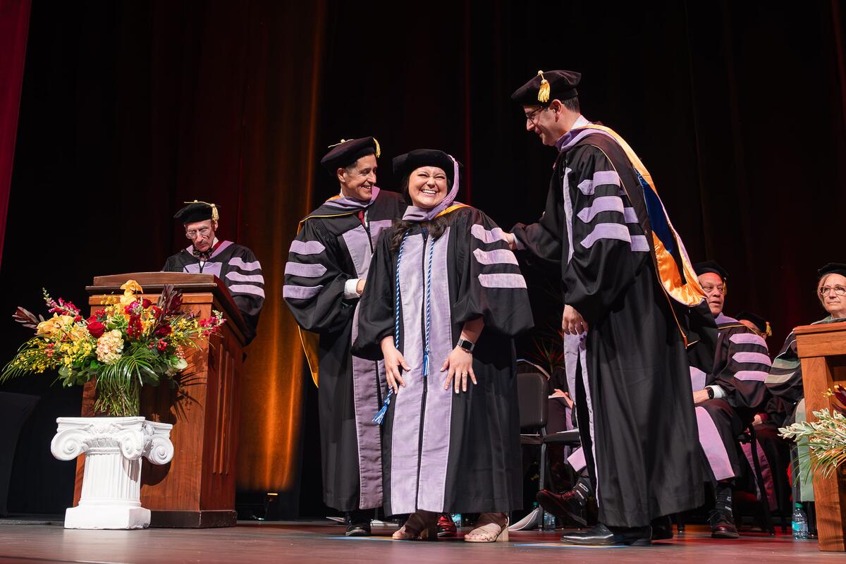 A graduate smiles as she receives her doctoral hood