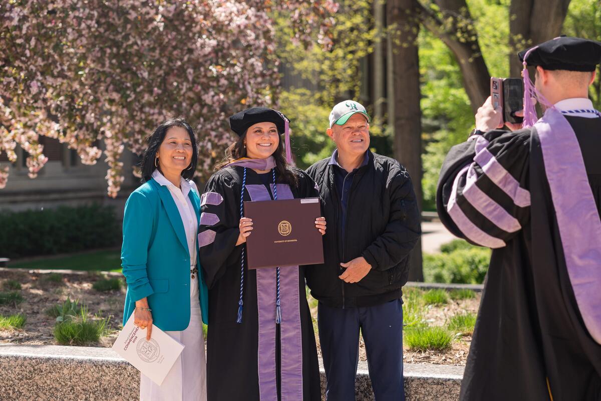A graduate poses with her family as another graduate takes their picture