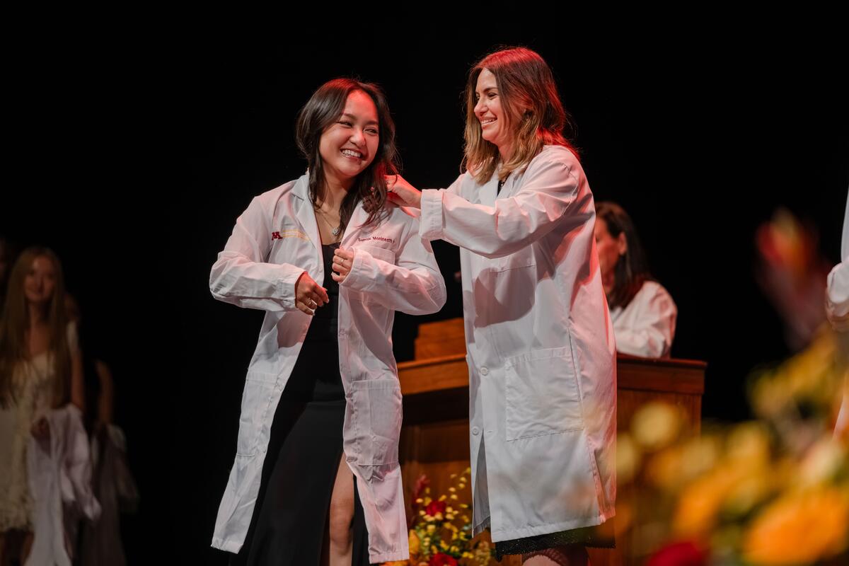 Student smiles and receives their white coat at the White Coat Ceremony
