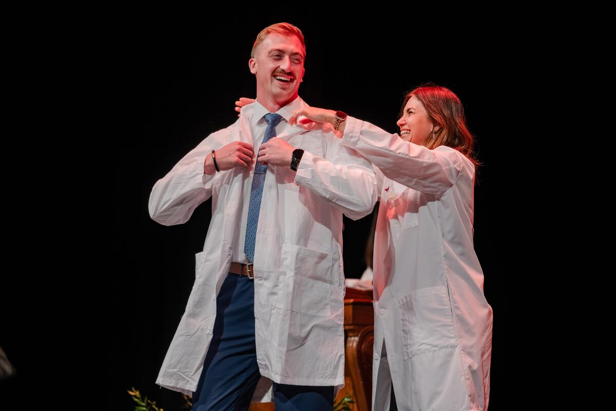 Student smiles and receives their white coat at the White Coat Ceremony