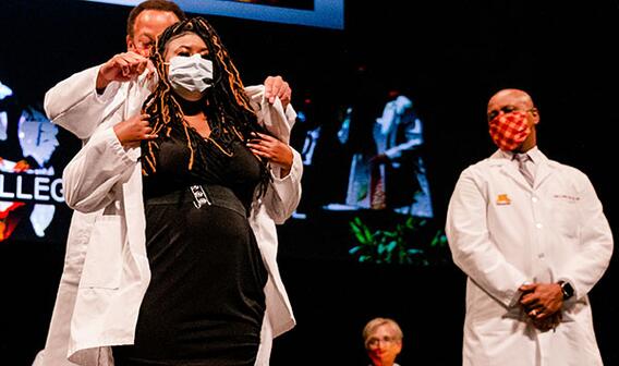 Second year student receives her White Coat from Dr. Karl Self and Dean Keith Mays looks on.