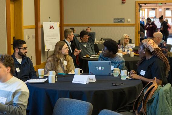 Student learners discuss research at a table with a laptop
