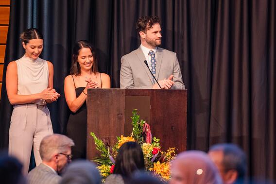 Class officers smile from behind a podium onstage