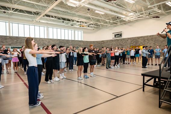 A large group of students engages in orientation activities, raising their arms for a game