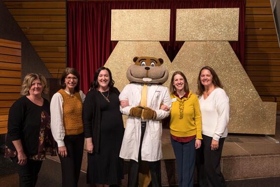 Members of the Development and Alumni Relations team pose with Goldy in front of an oversized block M