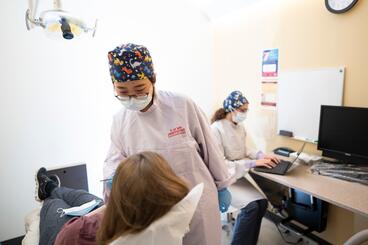 An orofacial pain specialist assesses a patient, while a second specialist sits at a computer in the background