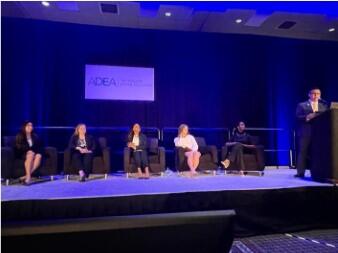 Presenter speaks on stage at ADEA with five others behind him