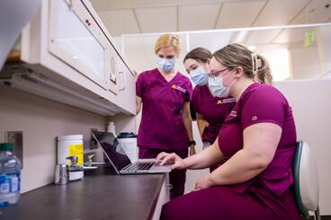 Three dental hygiene students look at a laptop in clinic