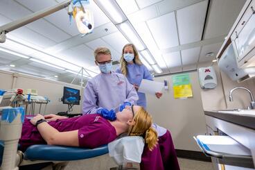 a dental hygiene masters student inspects a fellow student in clinic