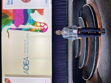 Yu Sun poses in front of an ADEA poster