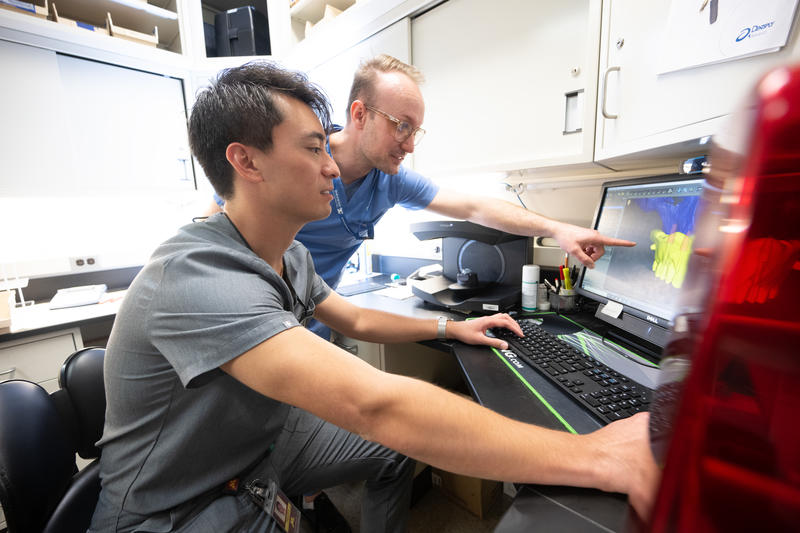 Prosthodontics residents Zane Clark and Tyson Merrill work with the 3D printer in the prosthodontics clinic.