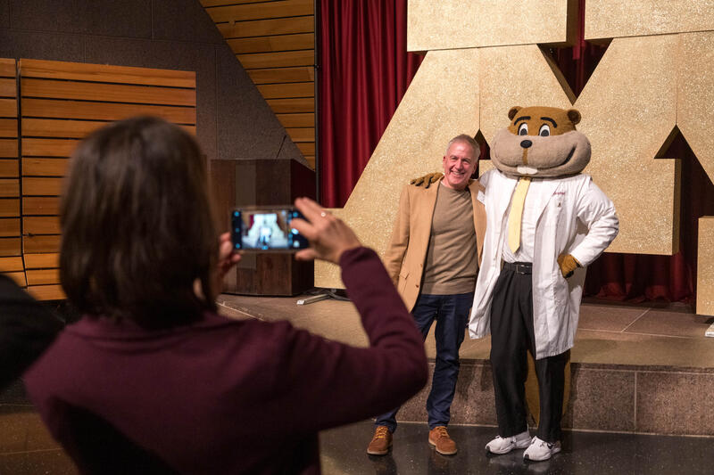 A School of Dentistry alumnus poses for a photo with a white coat wearing Goldy Gopher