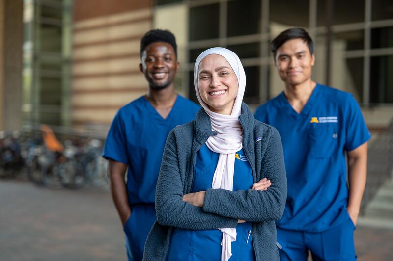 Three dental students pose in navy scrubs outside Moos Tower