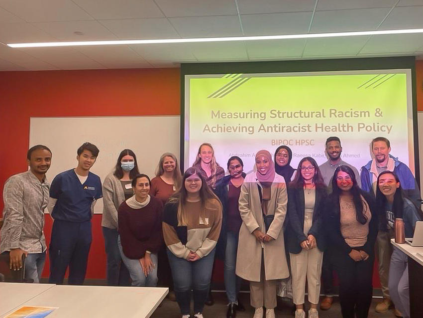 A group of learners poses in front of a presentation screen.