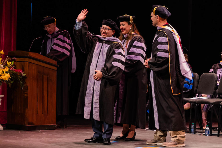 A graduate waves as his hood is placed