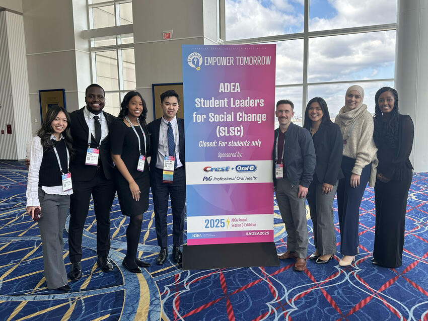 A group of students pose in front of a banner at ADEA