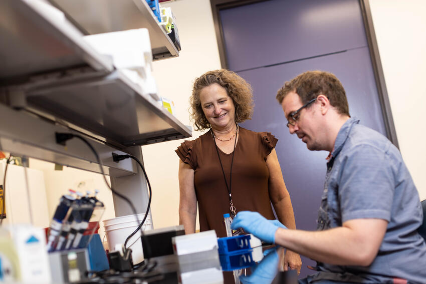 Kristin Artinger stands behind a researcher in the lab