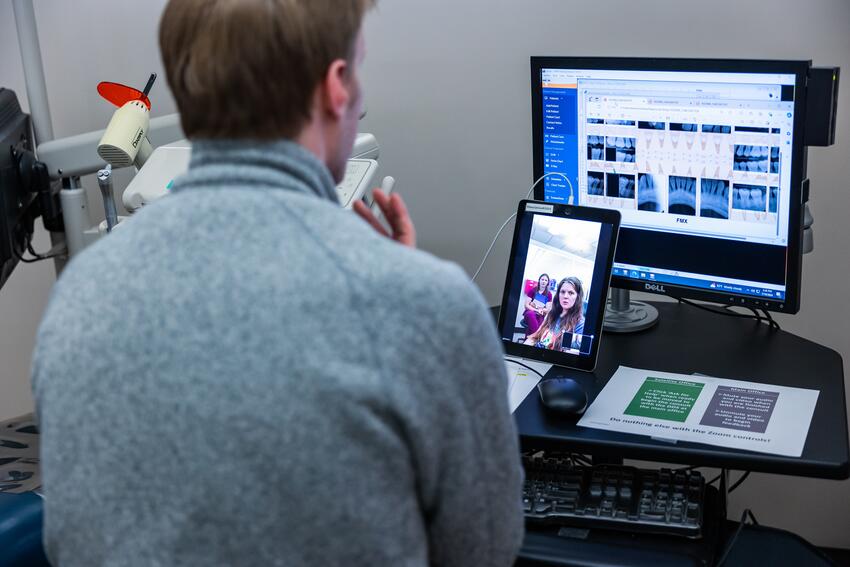 A DDS student engages in a teledentistry simulation, with a patient and a dental hygiene student on a tablet
