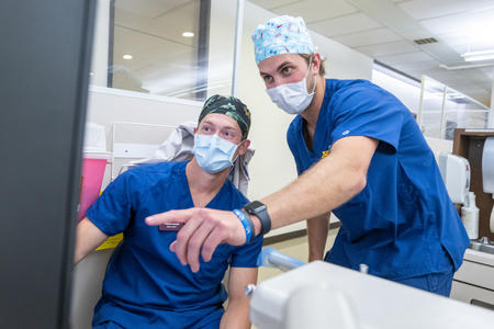 two DDS candidates point at a monitor in clinic wearing scrubs