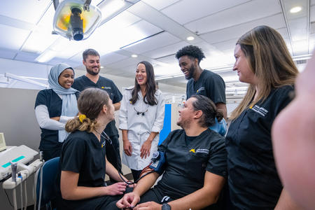 group of dental therapy students taking a student's blood pressure and laughing