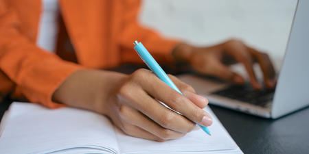 woman with laptop writing notes on paper