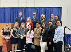 A group of 8 students and 6 faculty pose with awards 